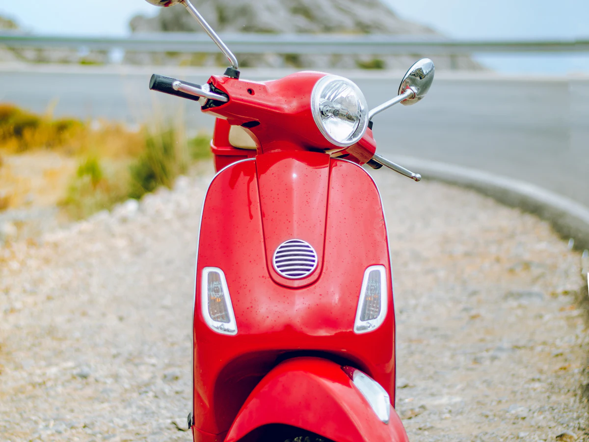 A red rental scooter parked by a coastal road